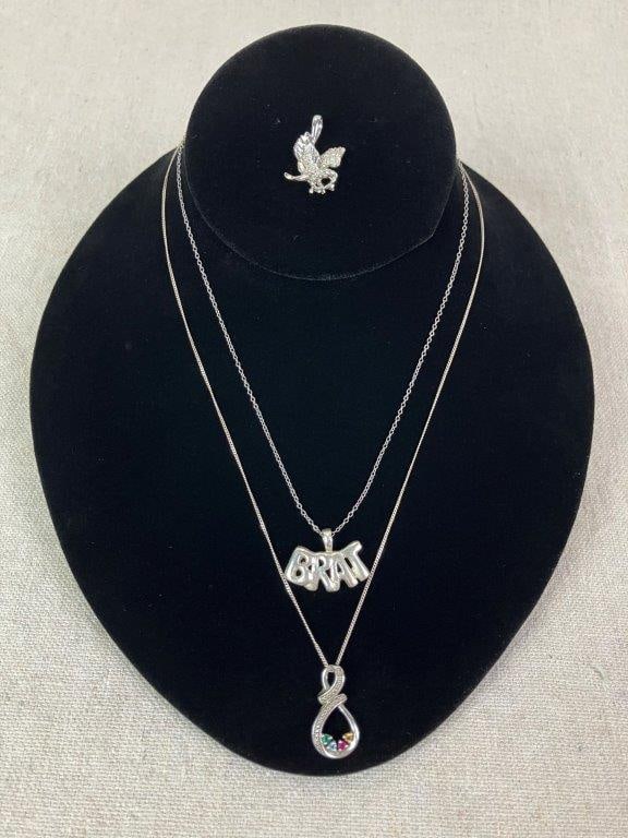 Jewelry Assortment Including Sterling Silver Necklaces: Assorted jewelry grouping including one silvertone eagle pendant necklace and two sterling silver necklaces, both marked for silver content. One sterling example features a "Brat" motto pendant measur
