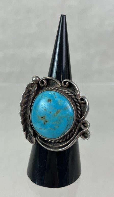 Native American Sterling Silver and Turquoise Ring: Artisan-crafted Native American ring featuring a central turquoise cabochon set within a robust sterling silver mount. Detailed with rope border, scrollwork, and feather motifs. Ring size approx. 6. U