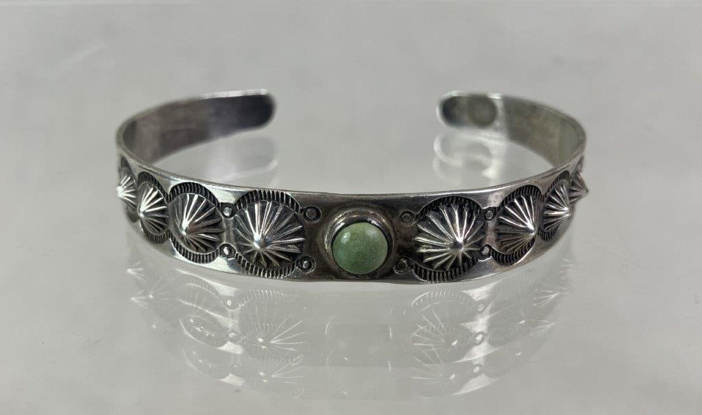 Native American Sterling Silver and Turquoise Cuff Bracelet: Native American cuff bracelet crafted in sterling silver, featuring a central green turquoise cabochon set within a stamped mount decorated with sunburst patterning, zigzag mountain motifs, and