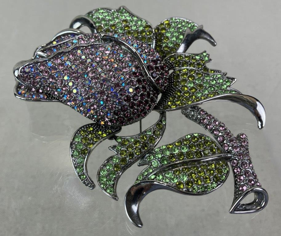 Massive Costume Jewelry Silvertone and Rhinestone-Style Rose Brooch: Substantial silvertone brooch designed as a blooming rose accented with green leafy adornments and stem, set throughout with a multitude of faceted rhinestone-style stones for dramatic sparkle.