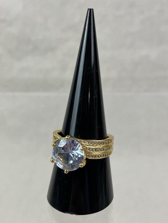 Sterling Silver Cocktail Ring: Sterling silver ring with goldtone finish featuring a central light blue brilliant-cut faceted stone of substantial presence, surrounded by a band set with a multitude of smaller faceted stones. Ring