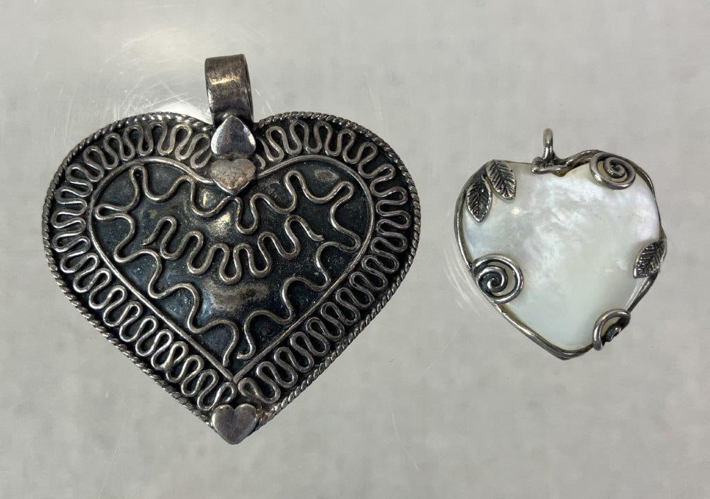 Two Sterling Silver Heart Pendants: Pair of sterling silver heart pendants, both marked for silver content to reverse. One features decorative embossed scrollwork to the surface, and the other centers a mother-of-pearl panel framed by
