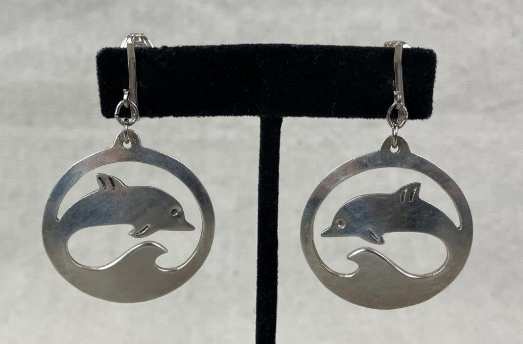 Taxco Sterling Silver Dolphin Dangle Earrings: Artisan-crafted Taxco sterling silver dangle earrings featuring stylized dolphins swimming within wave motifs. Marked for maker and silver content to reverse. One earring measures approx. 1 3/8"