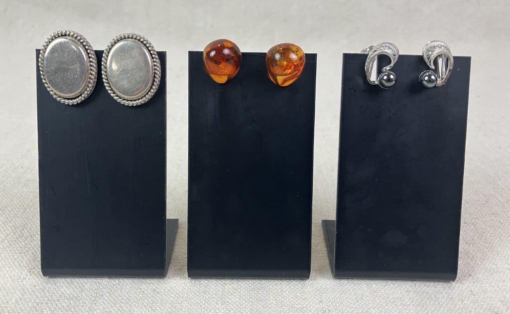 Three Pairs of Sterling Silver Earrings: Grouping of three pairs of sterling silver earrings including one pair of amber clip-on earrings, one pair of simple oval clip-ons with rope-design frames, and one pair featuring reticulated