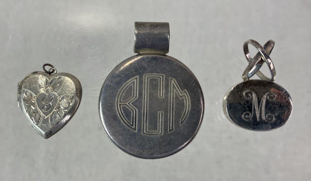 Sterling Silver Monogrammed Pendant Trio: Grouping of three sterling silver pendants, each monogrammed. Includes one antique locket engraved with a central monogrammed letter and surrounded by chased scrollwork decoration, one pendant by Morg