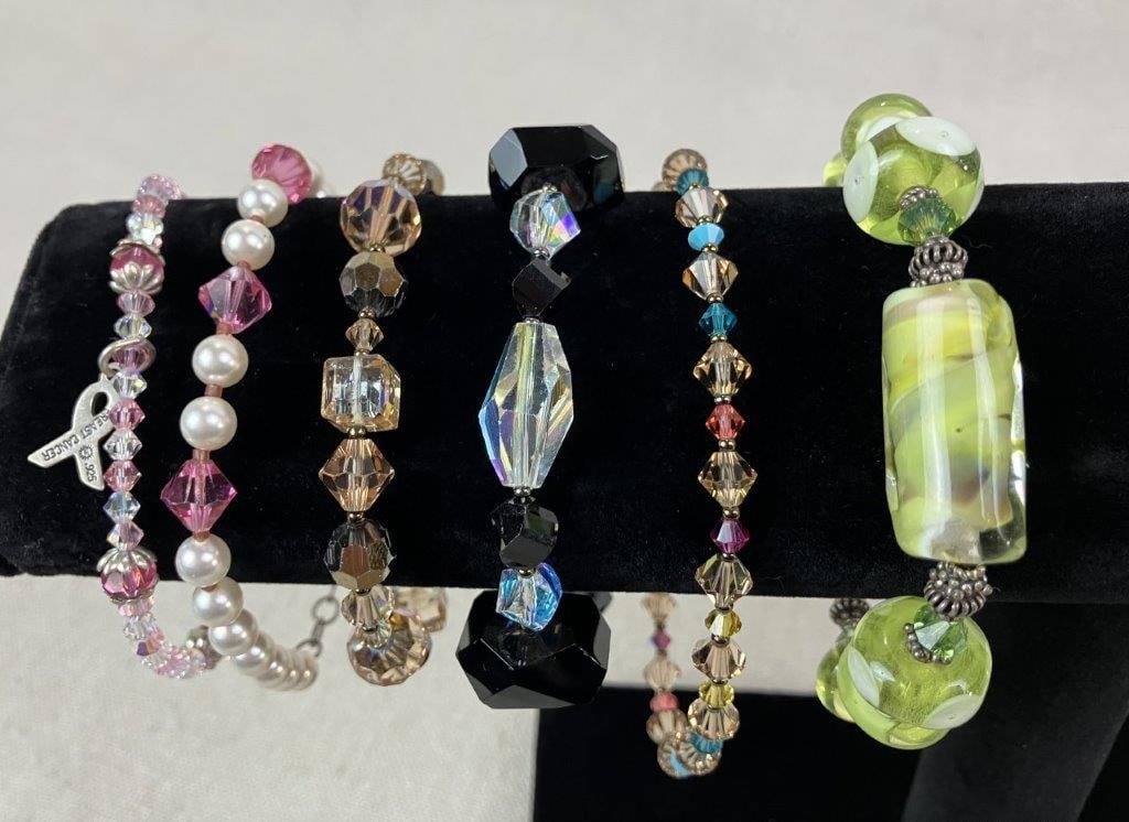 Six Beaded Bracelets: Collection of six beaded bracelets composed of multicolored faceted acrylic beads in varied designs. Highlighted by one standout bracelet featuring soft green art glass beads secured with a