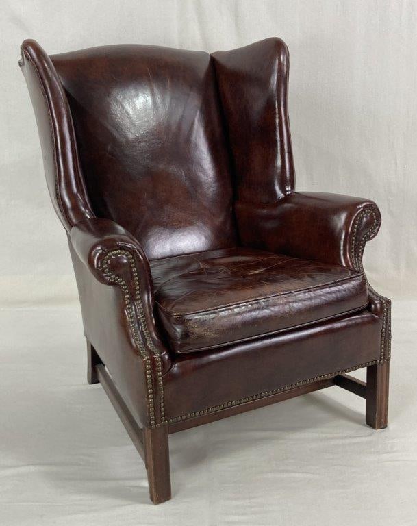 Leather Wingback Chair: A classic wingback armchair upholstered in warm mocha-toned brown leather featuring beautiful natural grain variation. The silhouette is accented with traditional brass-toned nailhead trim and