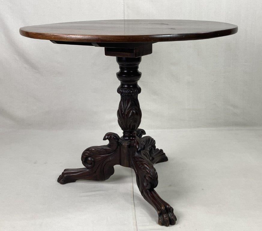Carved 19th Century Center Table: An ornate and substantial furniture piece featuring a heavily carved pedestal base embellished with lush acanthus leaf motifs and terminating in classic paw feet. The table is finished in a rich dark