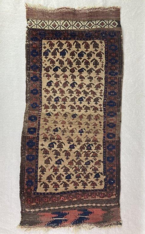 Antique Persian Rug: A hand-knotted Baluch rug featuring an ivory-colored field with red and blue accents arranged in a repeating pattern of geometric motifs. The rug retains a worn aged patina with frayed edges