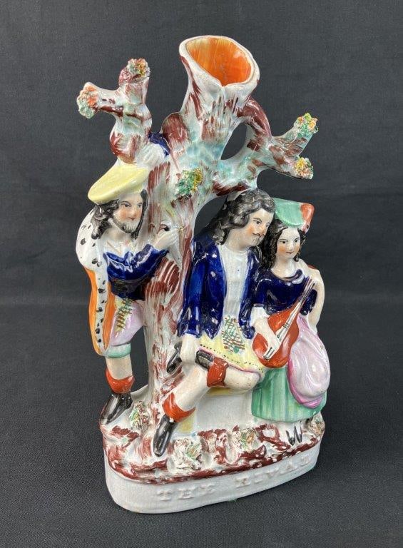 Staffordshire The Lover's Rival Spill Vase: Depicts two lovers beneath a verdant tree in traditional English dress, the female figure playing a stringed musical instrument while a rival or onlooker peers from around the tree. Decorated in