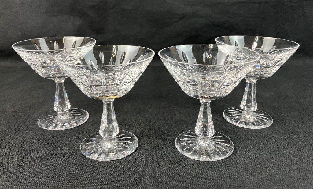 Four Waterford Crystal Kylemore Champagne Glasses: Waterford crystal with a luminous clear surface and distinctive cut decoration featuring starburst patterns. Suitable for serving champagne or sherbet. One glass measures approximately 4 3/4" H x 4