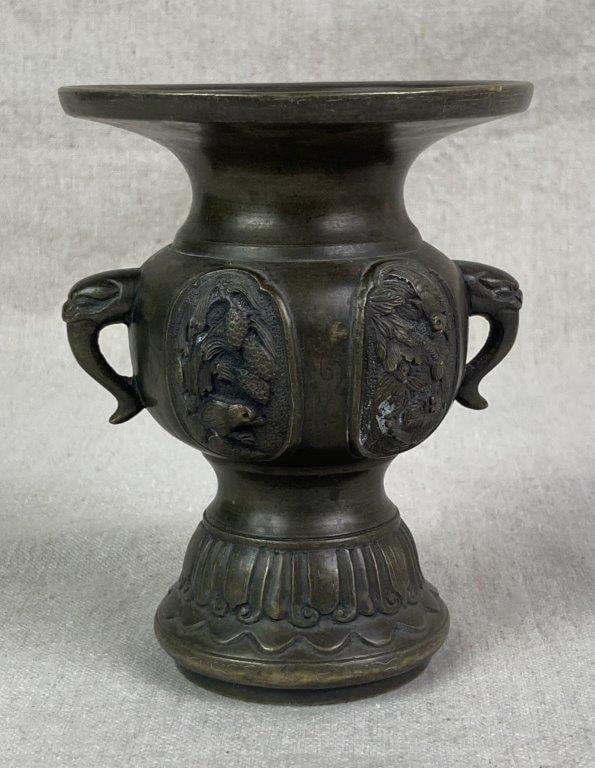 Late 19th Century Japanese Usubata Vase: A bronze usubata vase featuring lion head motif handles and ornate relief panels on each side depicting floral and bird scenes, raised on a pedestal base. The underside bears the maker's name, and