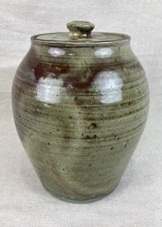 North Carolina Studio Pottery Covered Jar: North Carolina studio pottery covered jar with traditional rounded form and fitted lid, finished in a soft green runny glaze over a brown ground. The vessel displays a graceful curving profile with