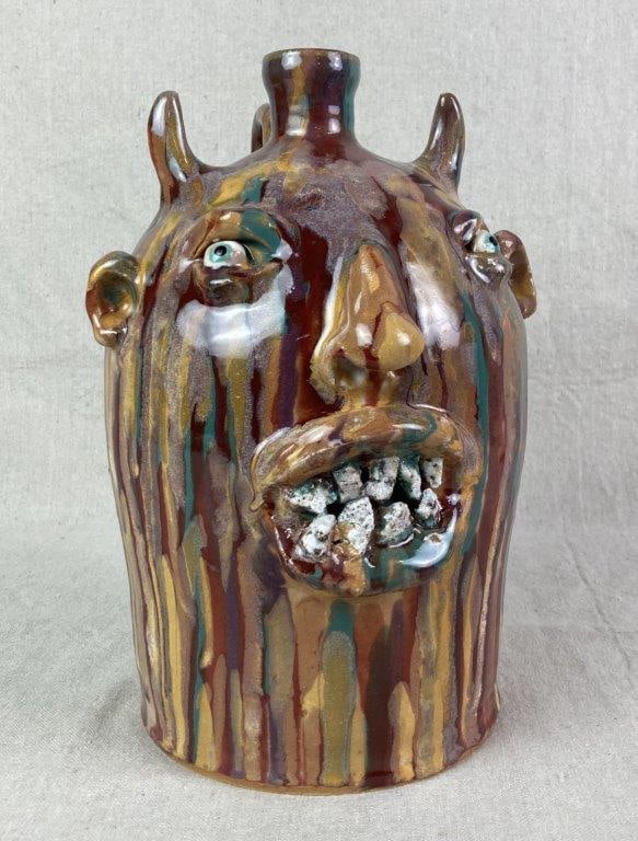 Devil Face Jug by Marvin Bailey: Southern stoneware face jug featuring applied horns, eyes, ears, nose, and mouth, accented with inset stone teeth. The vessel is finished in a multi-colored glaze with characteristic vertical