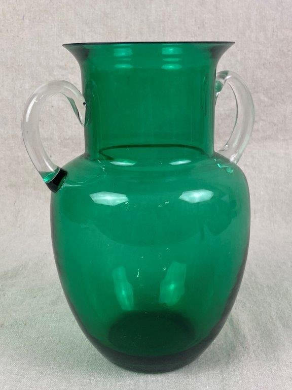 Green Art Glass Vase: A hand-blown decorative green art glass vase featuring a bulbous body, defined neck, and wide flared rim, accented by elegant applied handles in contrasting clear glass. Measures approximately 9