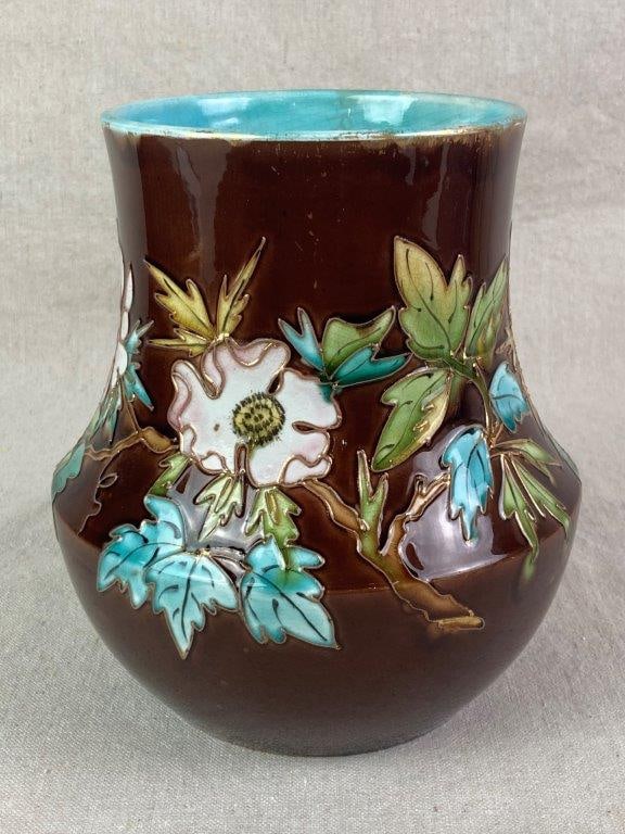 French Majolica Art Vase: A ceramic vase decorated in raised-relief with molded leaves and flowers set against a dark brown ground, featuring a contrasting turquoise blue interior. The base has a hole and bears the