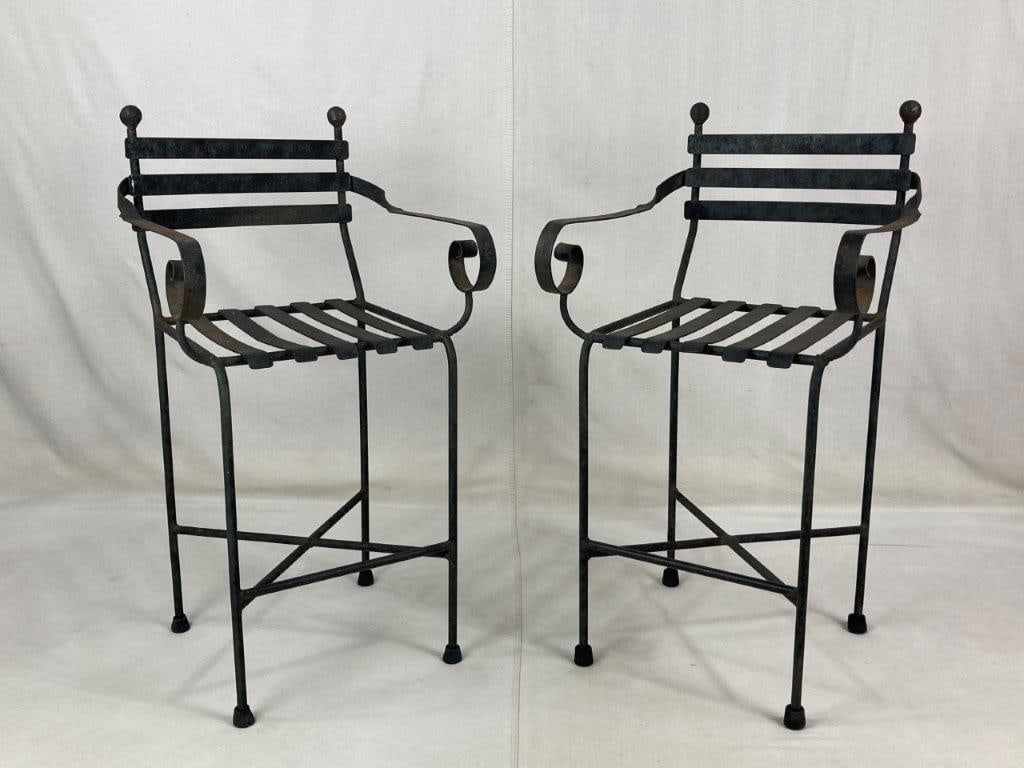 Pair of Iron Bistro Chairs: A pair of elevated wrought iron chairs featuring elegant curving scrollwork armrests and a slender, vertical form. The chairs are designed in a classic bistro style, suitable for patio or