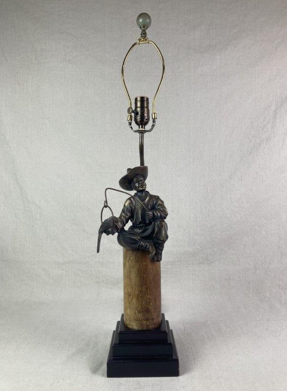 Bronze Figural Lamp: bronze figure of a seated man with a wide-brimmed hat holding a yoke from which a perched bird suspended, the figure is seated on a poloished stone column with a yellowish-brown mottled pattern,