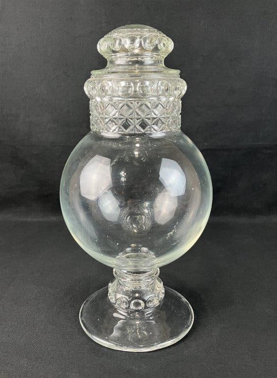 Glass Apothecary Jar: Traditional form with rounded body and decorative patterning near the top, accompanied by a coordinating cover. Pressed glass construction. Measures approximately 14 1/4â€³ H x