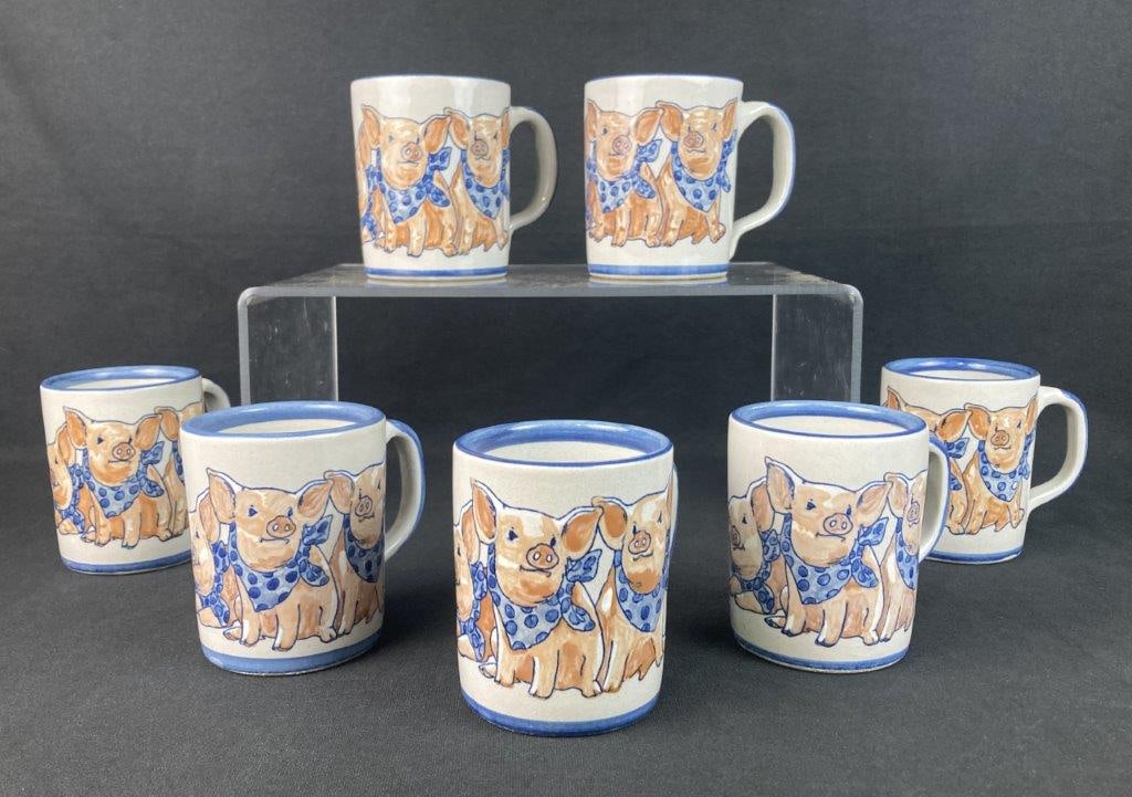 Louisville Stoneware Precious Pig Mugs: Set of seven hand-painted stoneware mugs, each decorated with three pigs wearing blue polka-dot bandanas. Unified by bold, hand-brushed cobalt blue accents on the rims and handles, with bases