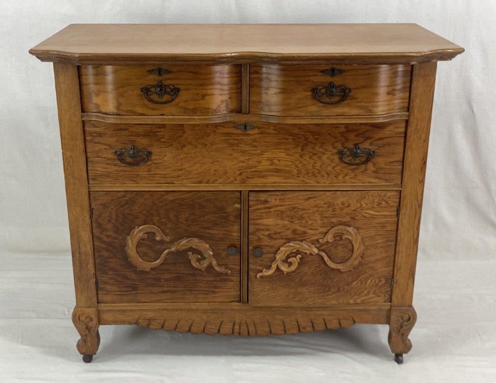 Oak Server: Late 19th Early 20th Century, an oak sideboard or server featuring serpentine-front drawers fitted with decorated hardware. The piece is embellished with carved wood appliques in vegetal and leafy