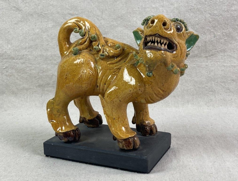 Foo Lion Pottery Figure: A ceramic foo lion figure decorated in a distinctive palette of mustard yellow, green, and brown, mounted on a solid black base. Measures approximately 7 1/2'' H x 7 1/2'' W x 4'' D, Good condition. 