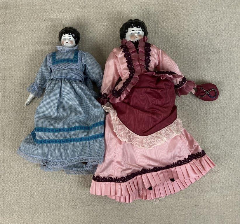 Two German China Dolls: Pair of German china head dolls with molded black hair and hand-painted facial features including blue eyes. One doll is dressed in a Victorian-style gown in bright pink tones with lace accents,