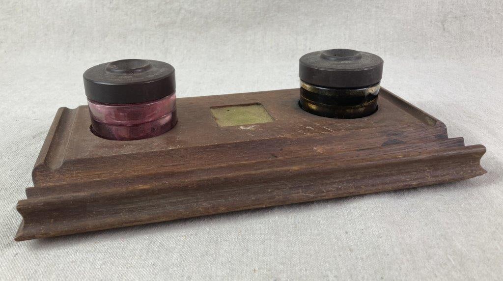 Sengbusch Ink Wells with Stand: Antique double self-closing inkwells by Sengbusch set into a carved wood base. The stand includes two circular wells and an integrated groove for holding pens, all exhibiting a worn aged patina.