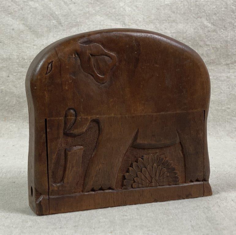 Folk Art Carved Cigarette Box: A wood cigarette box featuring a carved elephant design with a floral motif below, finished in a dark tone. The hinged lid opens to reveal twenty cigarette compartments. Measures approximately 5'' H