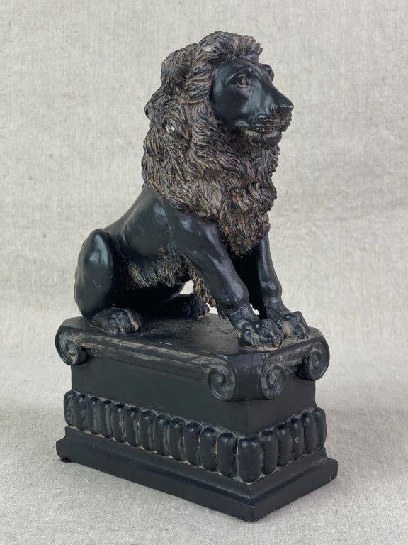 Vintage Chalkware Lion Statue: Chalkware statue depicting a male lion in a seated pose on a classical-style plinth detailed with scrolls and a decorative frieze. Matte black finish with brown accents highlighting the