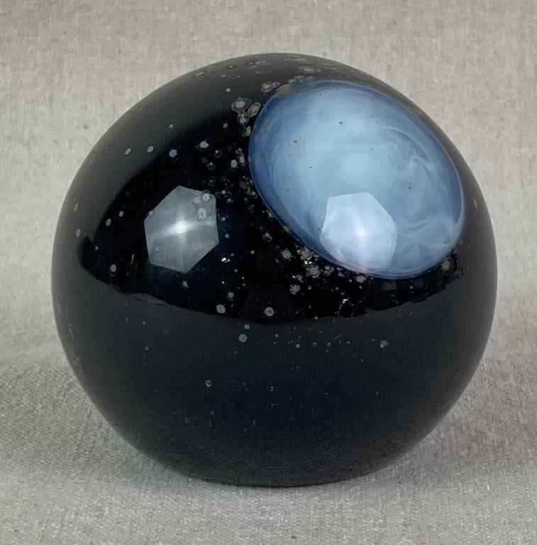Celestial Art Glass Paperweight: Captivating celestial-themed art glass paperweight featuring a deep black glass orb with a prominent planet-like circle of swirling white opalescent glass. Decorated with clusters of crystalline