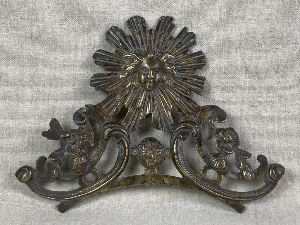 Louis XIV Sun King Wall Sculpture: Ornate brass furniture embellishment converted into a wall hanging, featuring a scrolling design with floral motifs surmounted by a Sun King emblem. Measures approximately 6 3/4â€³ H