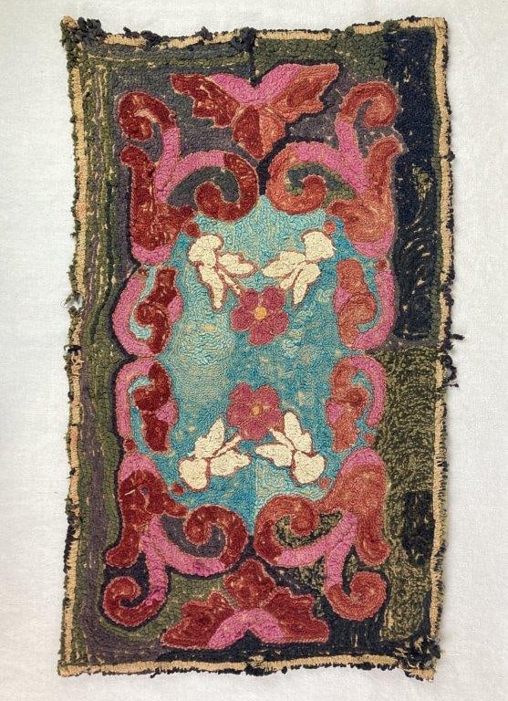 Folk Art Hand-hooked Rug: Antique hand-hooked rug featuring a central blue field with pink and white floral motifs and a pink and red scrolling border. Measures approximately 32â€³ L x 19â€³ W.