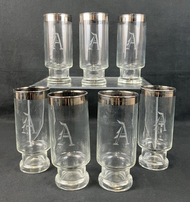 Seven Etched Glass and Silver Rimmed Highball Glasses: Anchor Hocking Bremen pattern highball glasses with etched “A” monogram and silver rims. One glass measures approximately 6 1/2″ H x 2 1/2″ diameter. Good condition with minor