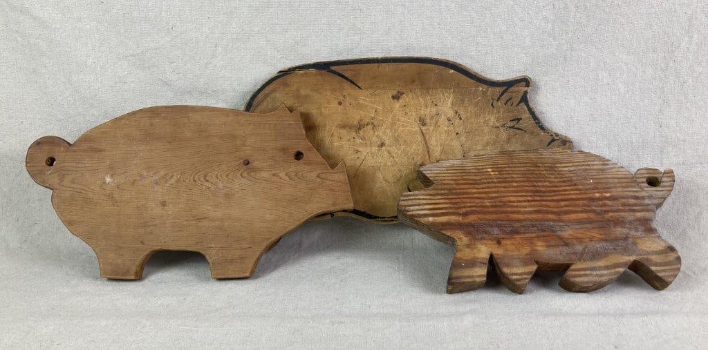 Wood Pig Cutting Boards: Three vintage wood cutting boards in the shape of a pig, including the largest example with a dark outline and another with a cutout eye, all with a worn aged patina. The largest measures