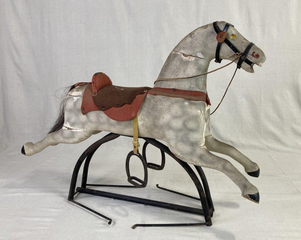 19th Century Rocking Horse: A hand-carved and painted wooden body suspended by a tubular metal swing frame. The horse retains charming period details, including expressive yellow gem eyes, a natural hair tail, and a fabric