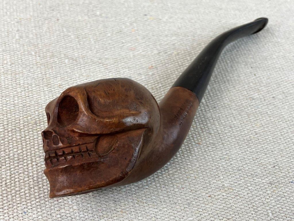 Briar Carved Figural Skull Pipe: Hand-carved figural pipe marked as genuine briar, featuring a sculptural skull head forming the bowl. The piece displays careful attention to detail with incised carving defining the facial structure