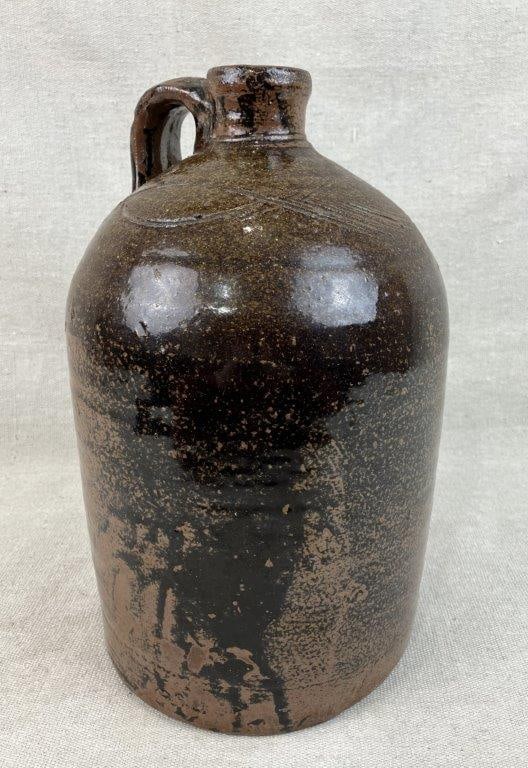 One Gallon Decorated Alkaline Glaze Stoneware Jug: This southern, likely Georgia or Alabama, jug features a traditional form with an applied strap handle and is finished in a glaze exhibiting natural beauty and subtle color variation. The shoulder of