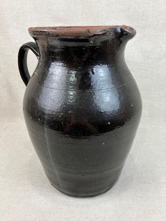 Hallie A. Wilson Stoneware Pitcher: Hall County, Georgia, 20th Century. This vessel features an applied handle, a flared lip, and a single incised band. It is finished in an Albany slip glaze and is marked with a "2" to indicate its
