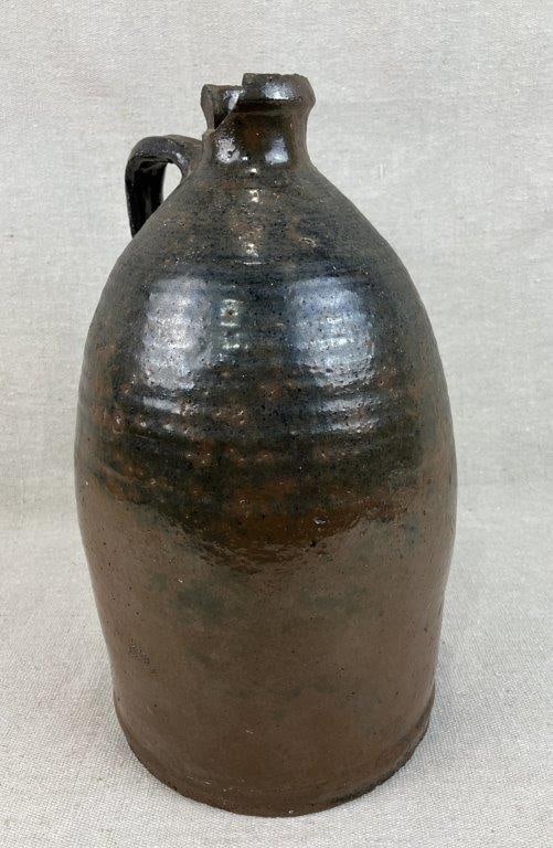Glazed Stoneware Jug: This piece features a traditional form with a defined lip and a slightly angular applied strap handle. It is finished in a rich, runny deep glaze—likely an Albany slip—that exhibits
