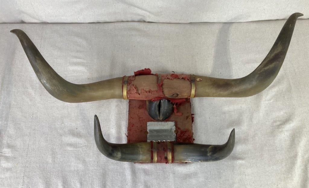 Folk Art Steer Horn Mirror: Two large, sweeping steer horns are anchored to a central natural wood log, positioned above a secondary tier of smaller horns that frame a central mirror and a single decorative hoof. The entire