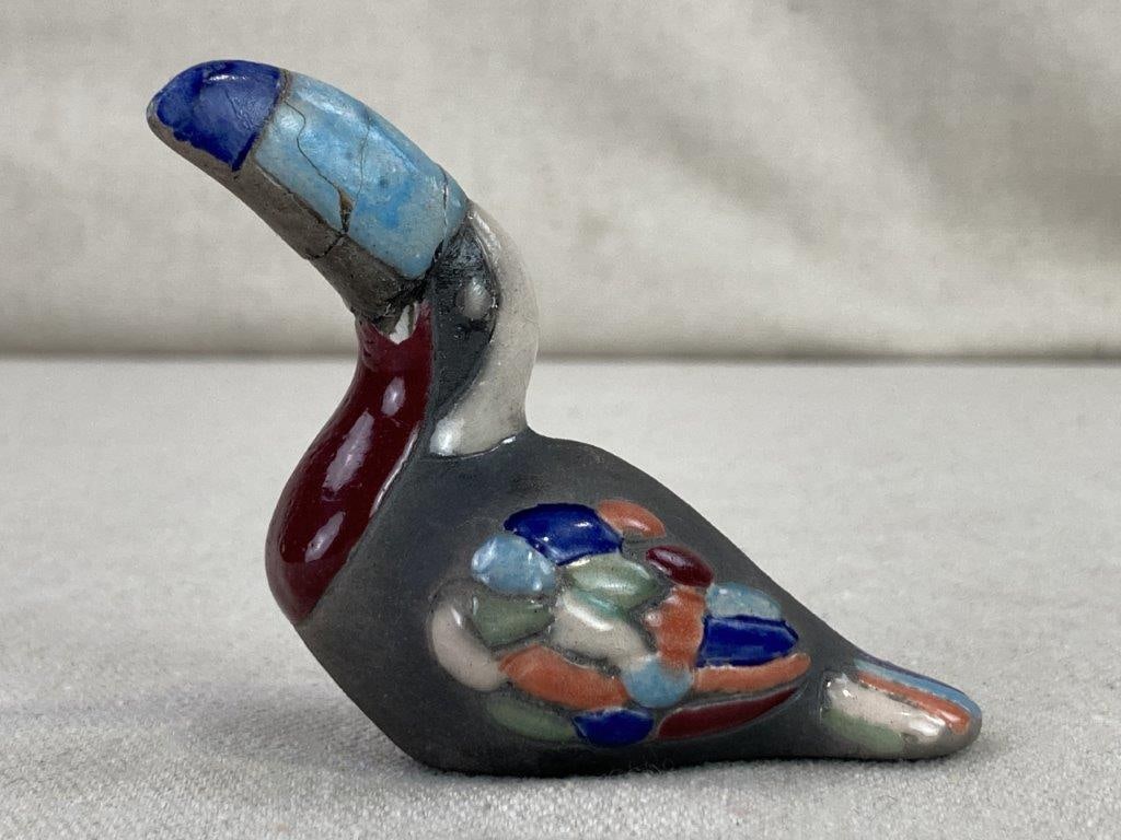 Ceramic Toucan Figure: A charming small ceramic figurine capturing the playful silhouette of a toucan, featuring a distinctive blue glazed beak and vibrant, multi-colored glazed feathers. The piece exhibits characterful