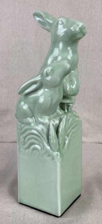Ceramic Rabbit Sculpture: This elegant figural piece is finished in a serene monochromatic celadon green glaze, depicting a pair of rabbits in a tiered, naturalistic composition. One rabbit is portrayed in an upright, alert