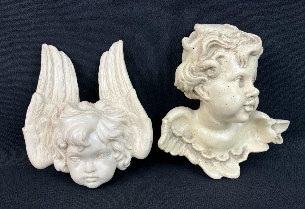 Two Angel Wall Plaque Sculptures: Wall plaque sculptures featuring the head of an angel with surrounding wings, cast in resin with molded detail. The piece displays a classical-inspired design suitable for decorative wall display.