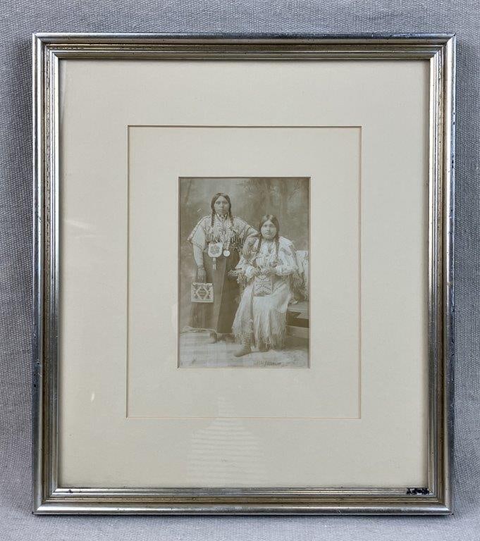 Native American Nez Perce Women Photograph: Photograph depicting two Nez Perce women in ceremonial attire, one seated and one standing, with expressive and contemplative features. Housed in a gilt frame. Frame measures approximately