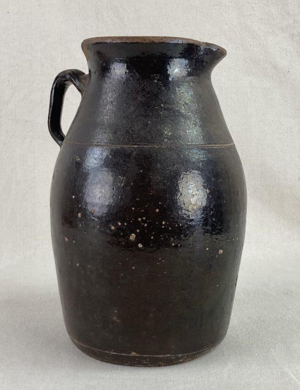Southern Stoneware Jug: This traditional Southern stoneware jug features a classic ovoid body that tapers to a lightly flared rim with a functional pinched spout. An applied strap handle connects the neck to the shoulder.