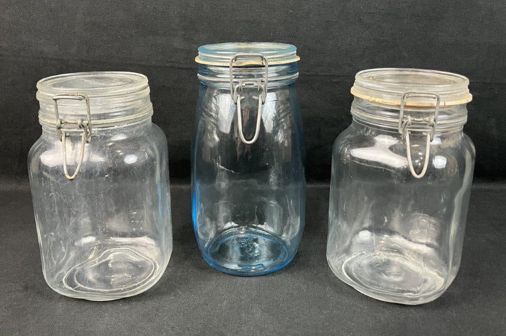 Glass Canisters: Group of three vintage glass canisters, including one blue glass example and two clear glass examples, each with hinged lids. The blue canister measures approximately 8 7/8â€³ H x