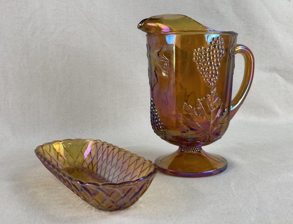 Carnival Glass Pitcher and Dish: A luminous set of gold-toned carnival glass featuring a vibrant iridescent finish. The collection includes a large pitcher detailed with an intricate grape and leaf motif, a classic pattern in early