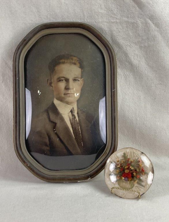 Early 20th Century Portrait of Man with Flower Display: This duo of antique wall decor captures the formal sentimentality of the early 1900s, pairing a striking portrait of a handsome young man in formal attire with a delicate botanical memento. The