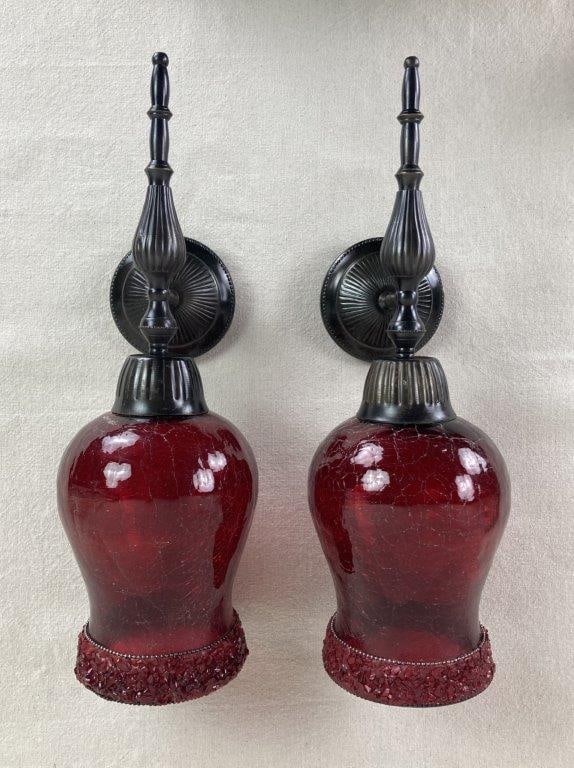 Red Art Glass Sconces: A striking pair of wall-mounted sconces featuring vibrant red crackle glass shades held by ornate bases with a ribbed, turned design. Each fixture is supported by a round wall mount, blending the